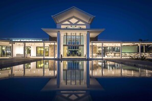 A modern hotel with a central atrium, a pool in the foreground, and multiple dining areas visible through the glass facade. - Taumeasina Island Resort (Apia)