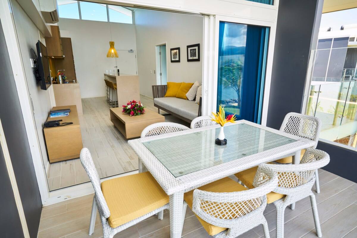 A modern living area with a glass-top table, wicker chairs, and a sofa with cushions.