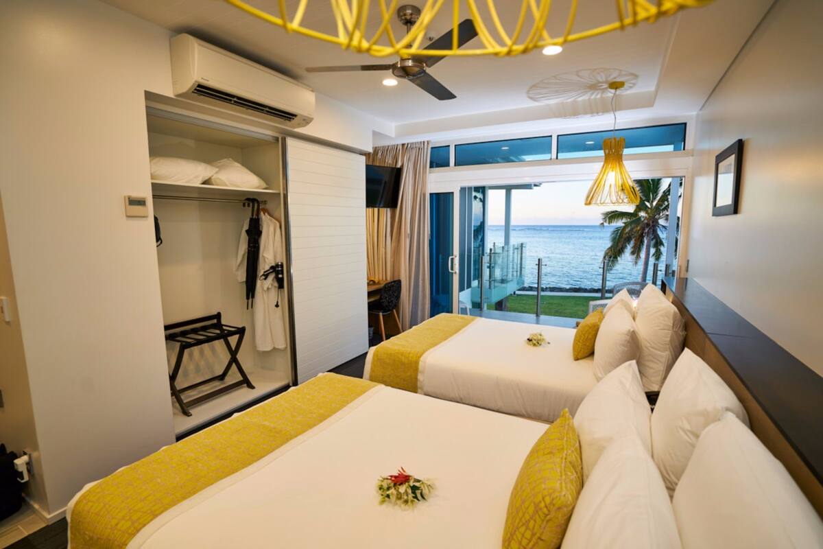 A hotel room with two beds, a balcony with a view of the sea, and an air conditioning unit.