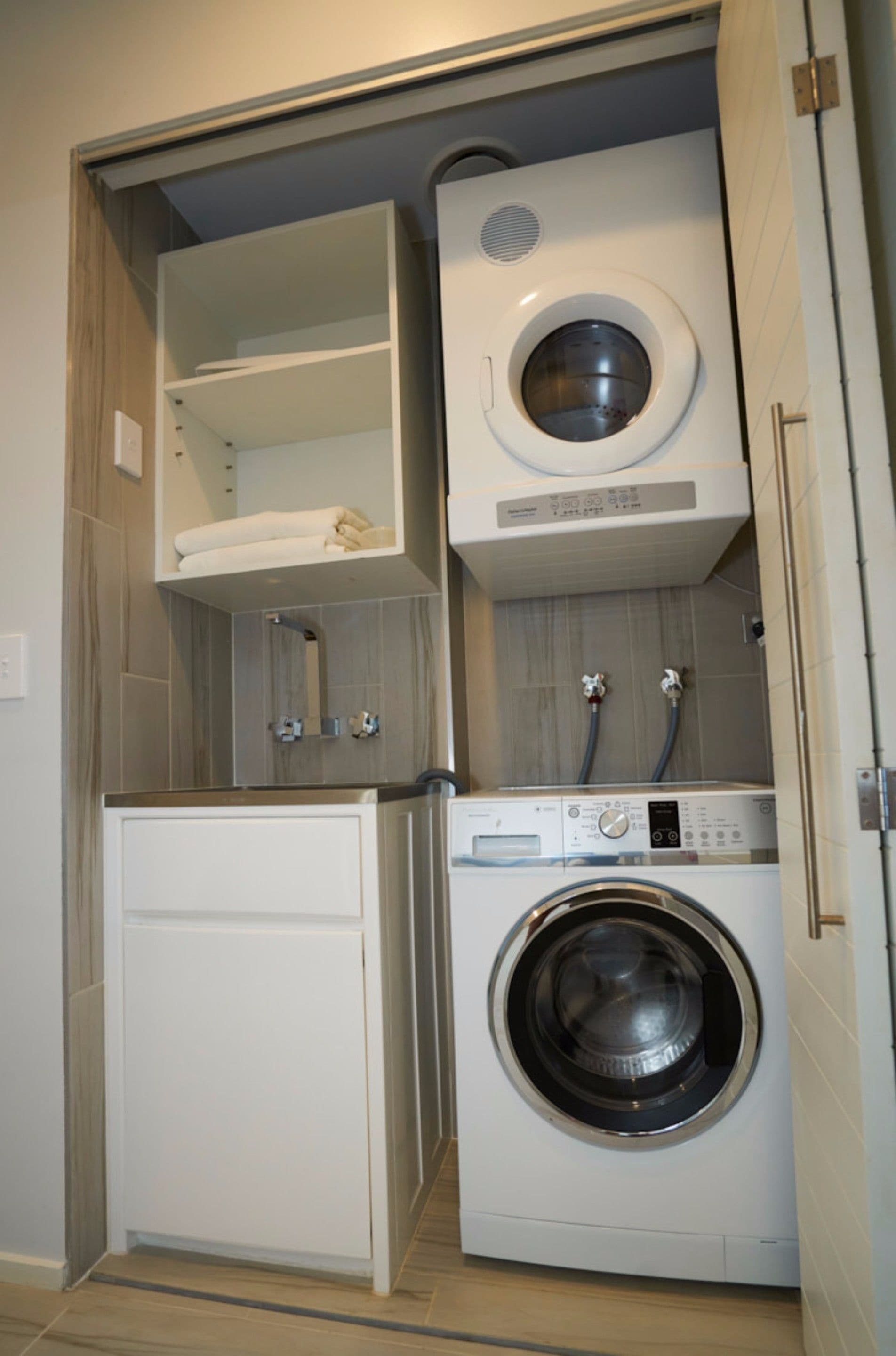 A compact laundry room with a washing machine, dryer, and shelving unit.