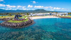 Een resort met een strand, helderblauw water en een bergachtige achtergrond.