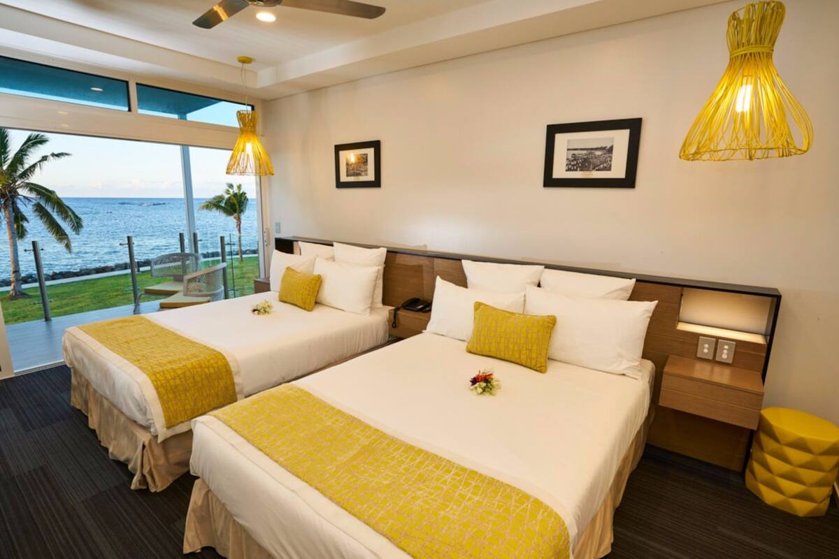 A hotel room with two beds, a balcony with a view of the ocean, and a yellow accent wall.