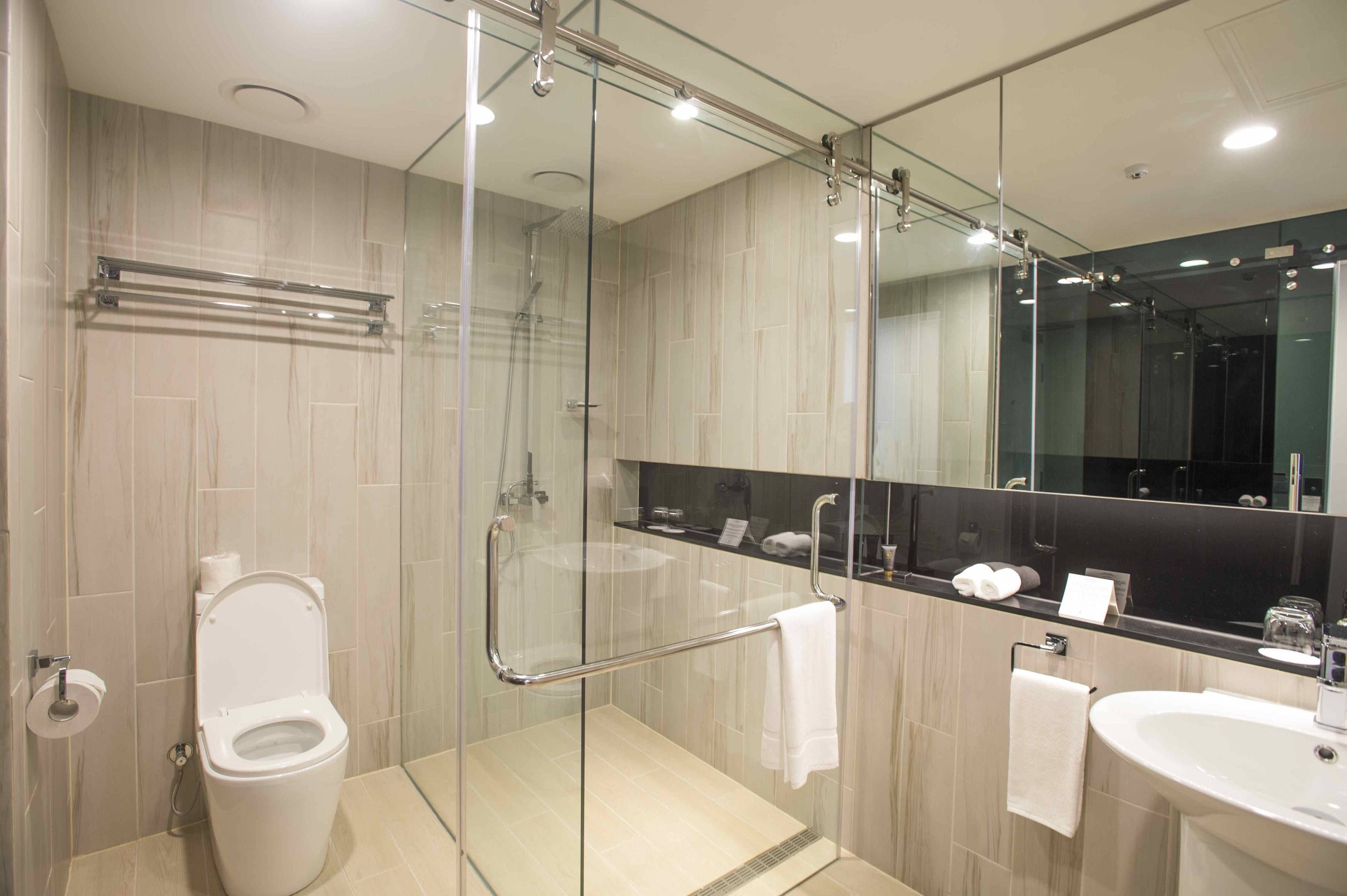 Un baño moderno con ducha de vidrio, inodoro, lavamanos y un espejo grande.