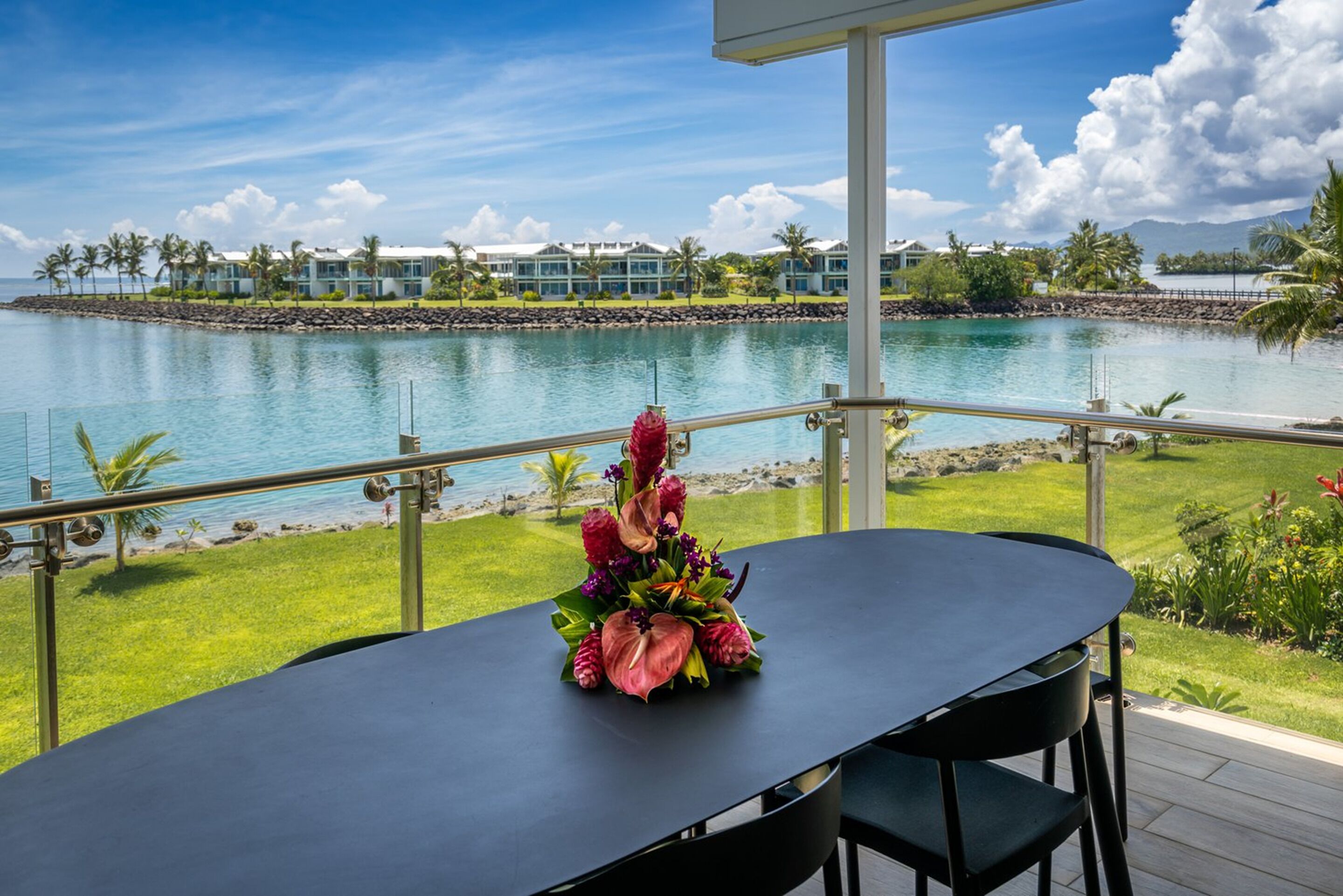 Una mesa con un centro de mesa floral en un balcón con vista a un cuerpo de agua, con un resort al fondo.
