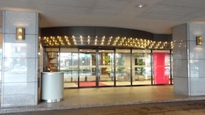 L’entrée d’un hôtel, avec une façade incurvée, des portes en verre et un mur d’accent rouge.