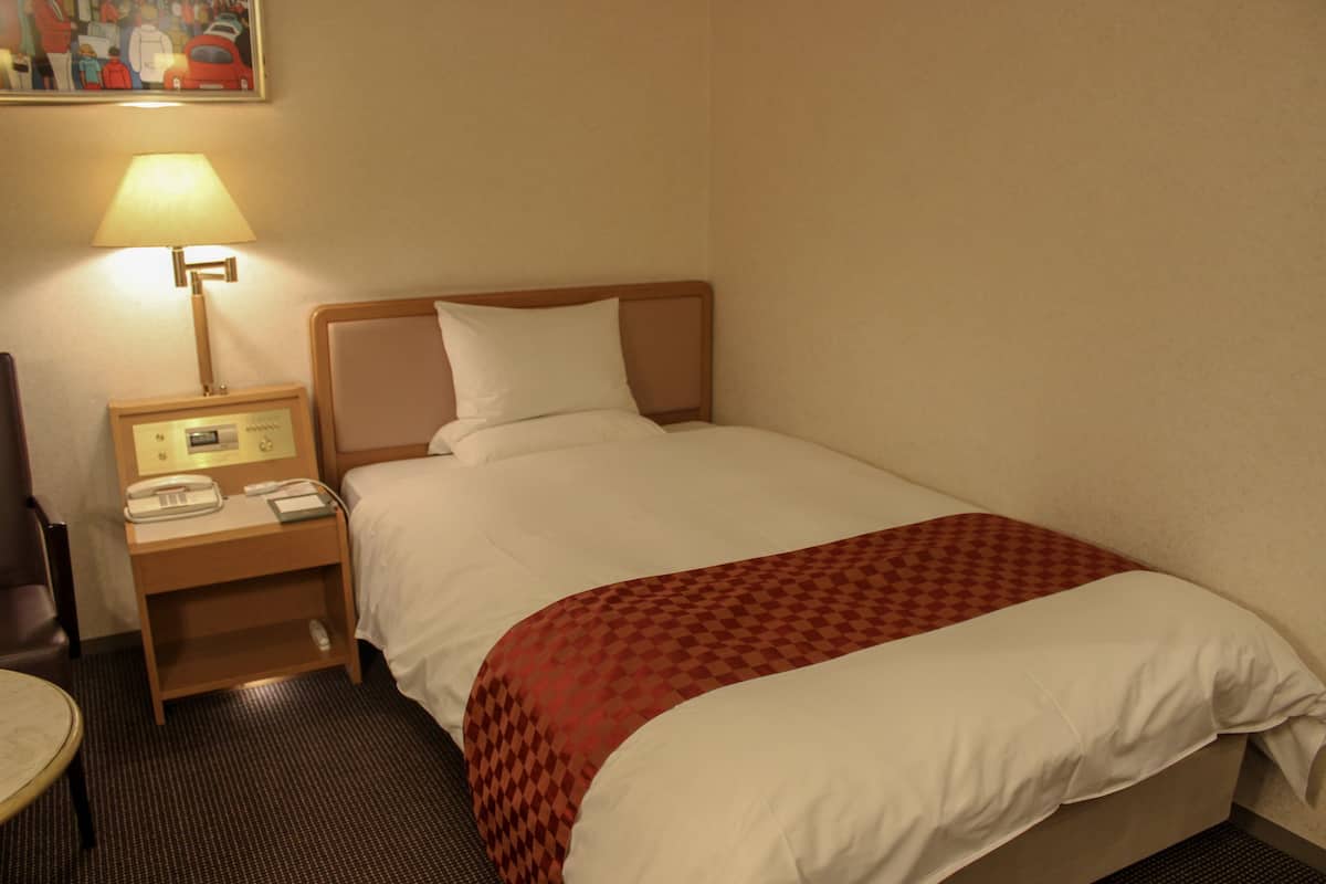 Una habitación de hotel con una cama, una mesita de noche con lámpara, un teléfono y una silla.