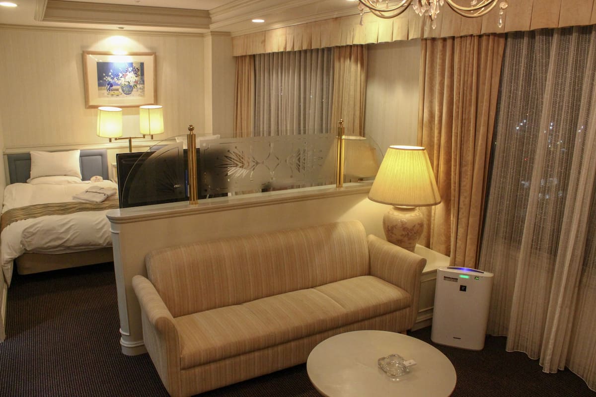 Una habitación de hotel con cama, sofá, mesa de centro, televisor y lámpara.