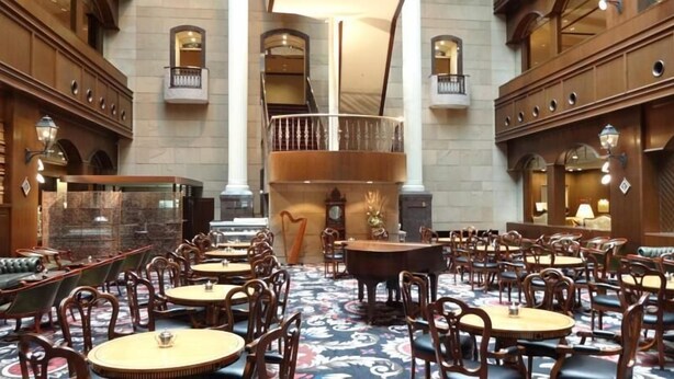 Un hall d’hôtel spacieux, doté de nombreuses tables et chaises rondes, d’un grand escalier et de détails architecturaux raffinés.