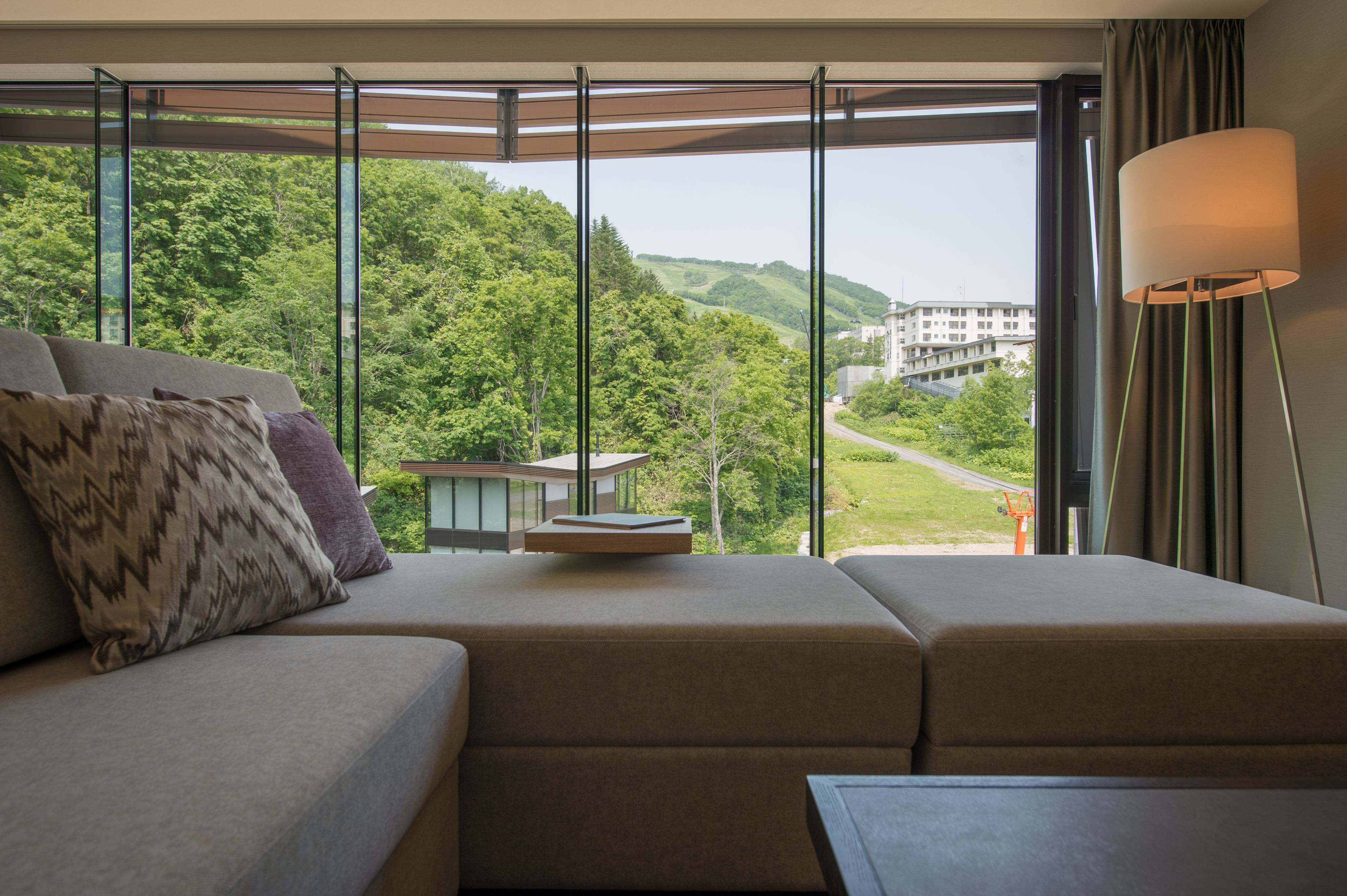 A modern hotel room with a large window offering a view of a lush green landscape and a building in the distance.