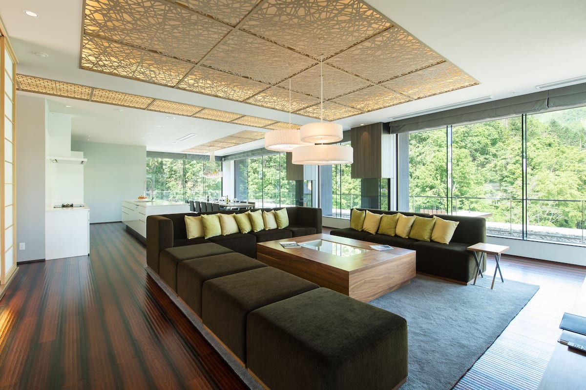 A modern living room with a sectional sofa, a coffee table, and a view of the outdoors through large windows.