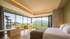 A modern hotel room with a large bed, a desk, and a view of the mountains.