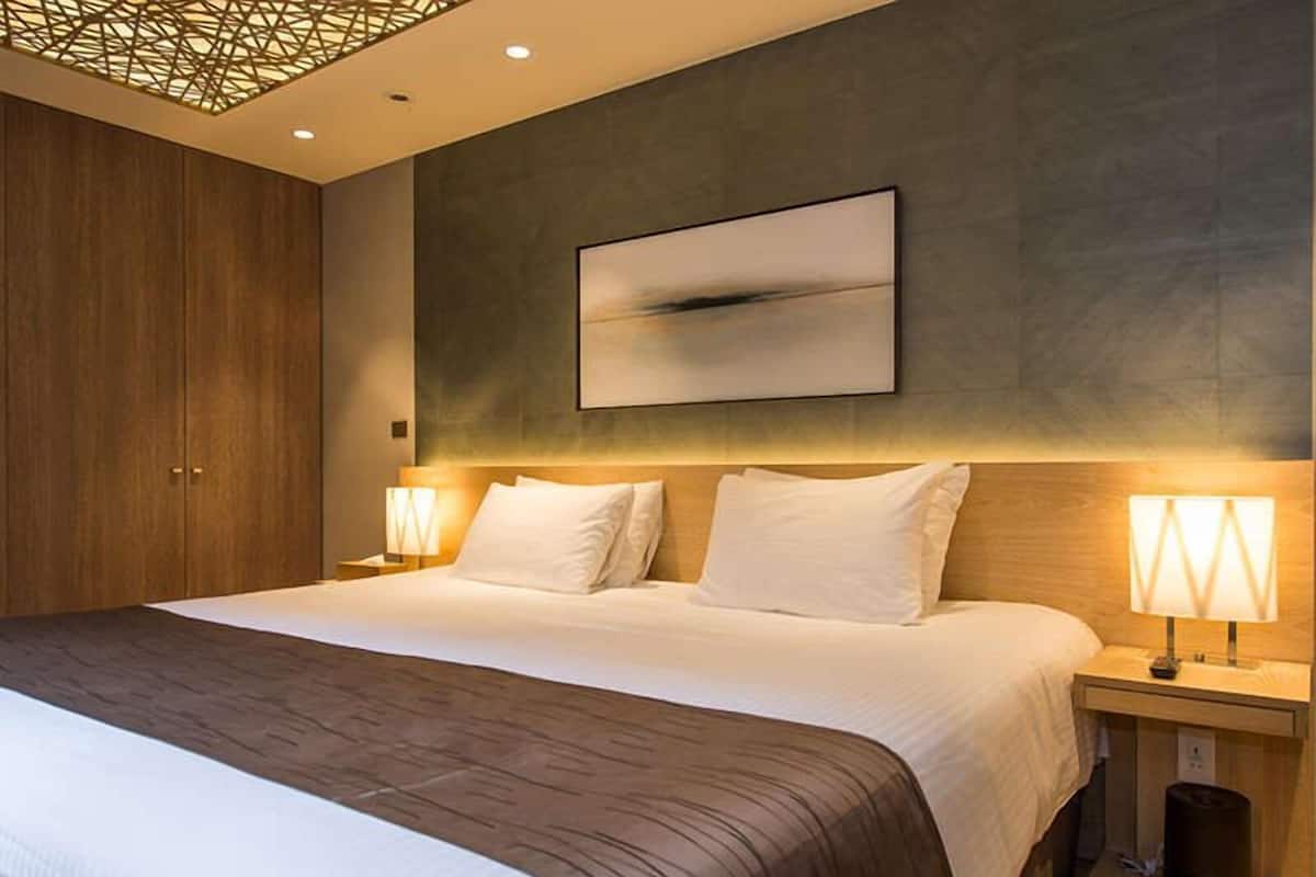 A modern hotel room with a large bed, wooden wardrobe, and a wall-mounted artwork.