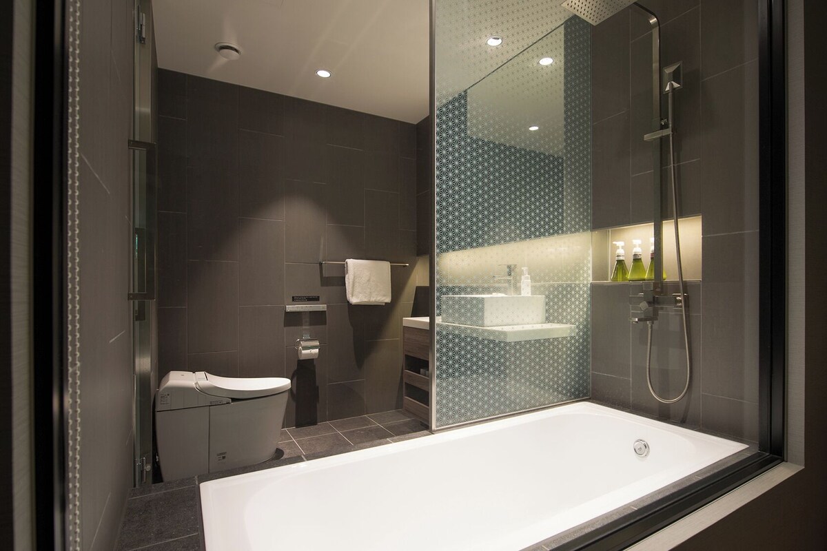 A modern bathroom with a bathtub, shower, toilet, and a glass-enclosed vanity area.