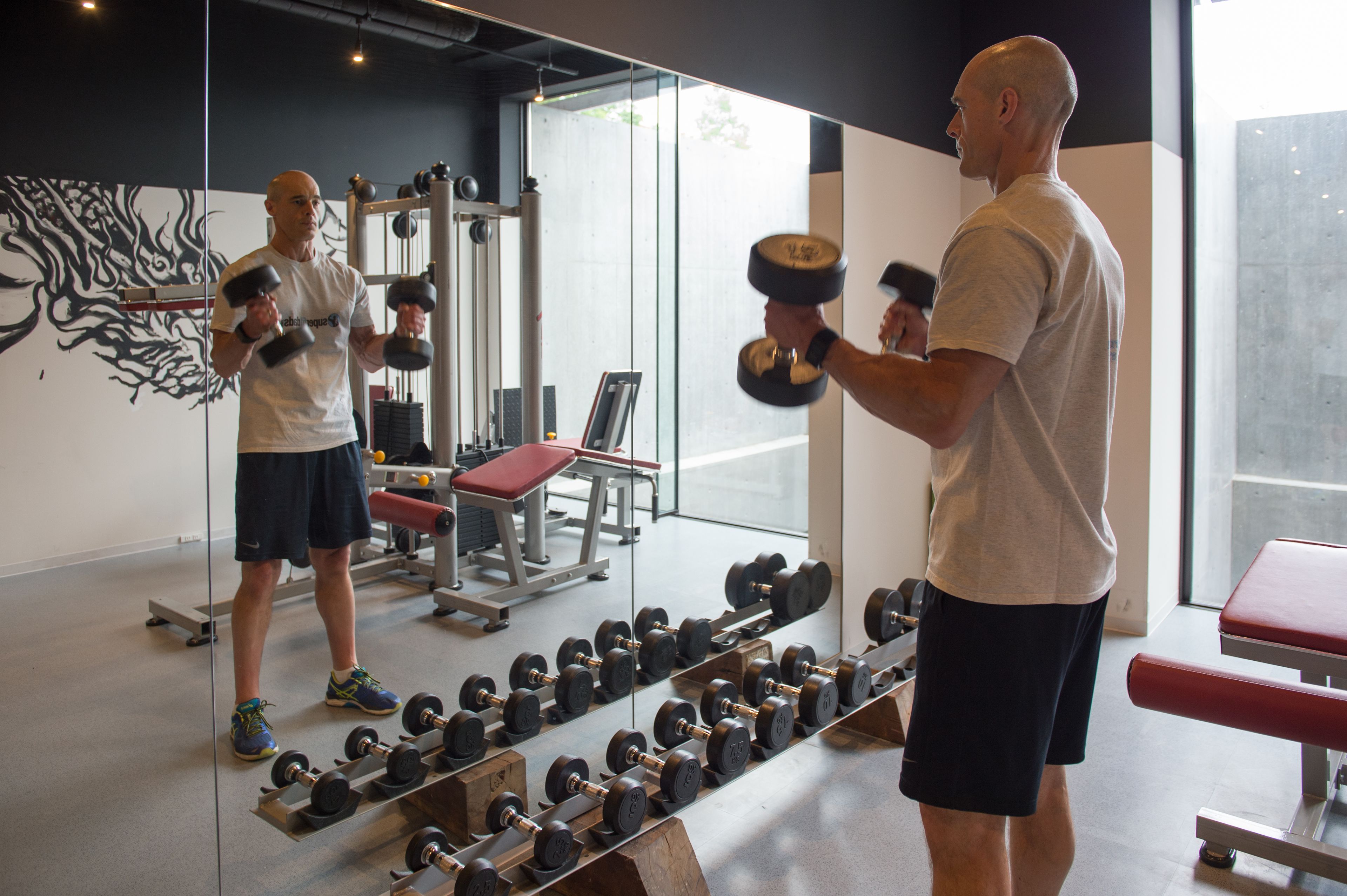A gym with weightlifting equipment, benches, and a mirror.