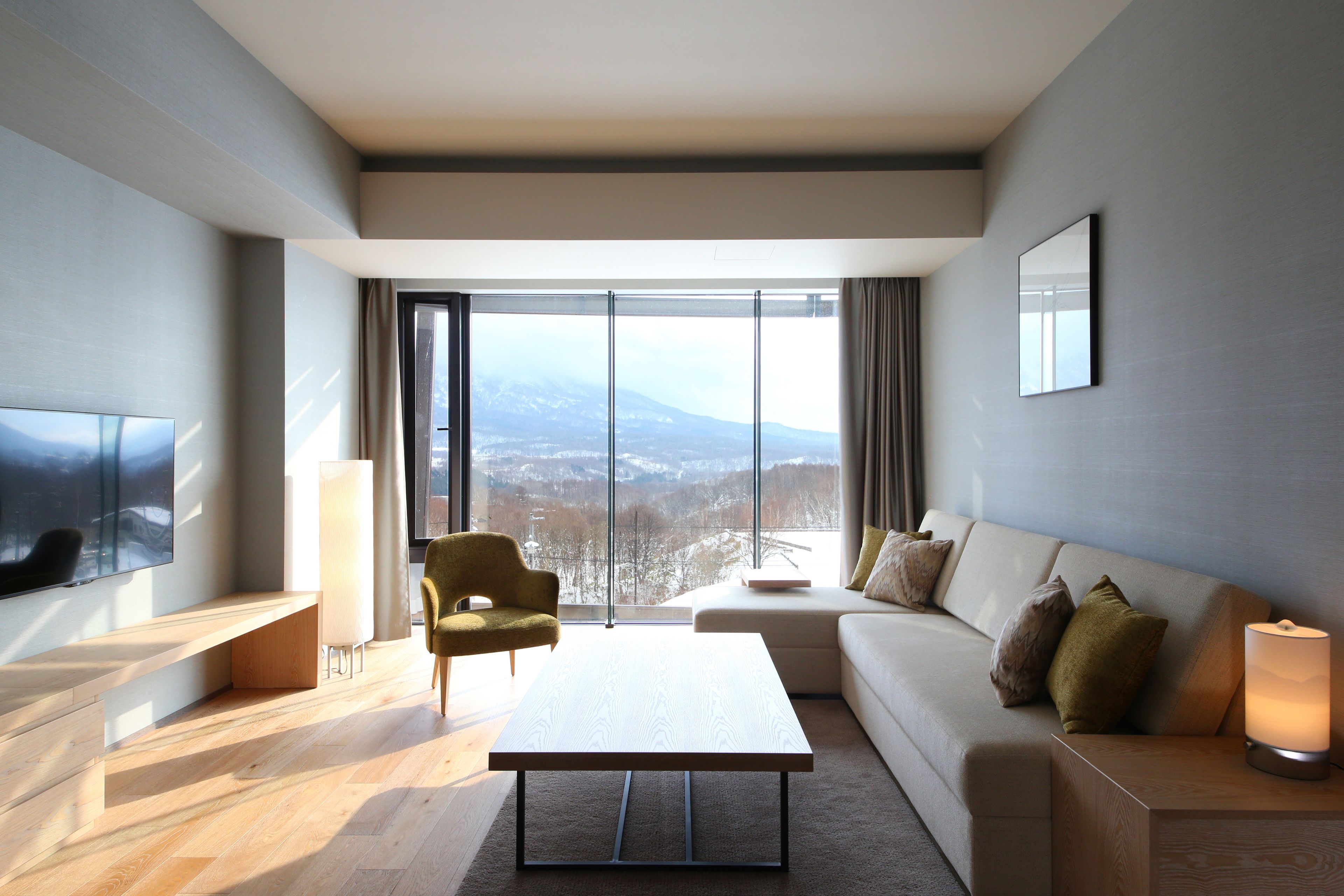 A modern living room with a large window, a sofa, a coffee table, and a TV.