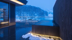 A modern building with a glass facade and a wooden exterior, featuring a snowy landscape and a view of a forested hill.
