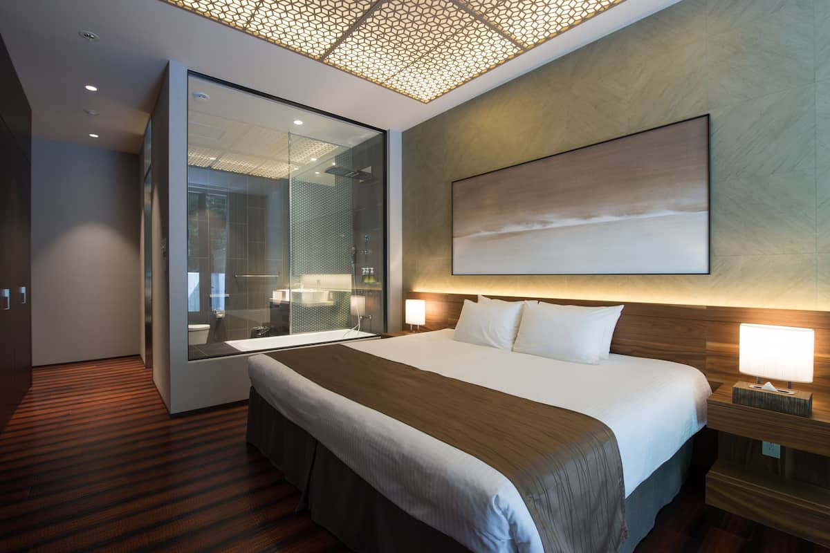 A modern hotel room with a large bed, a glass shower enclosure, and a large abstract painting on the wall.