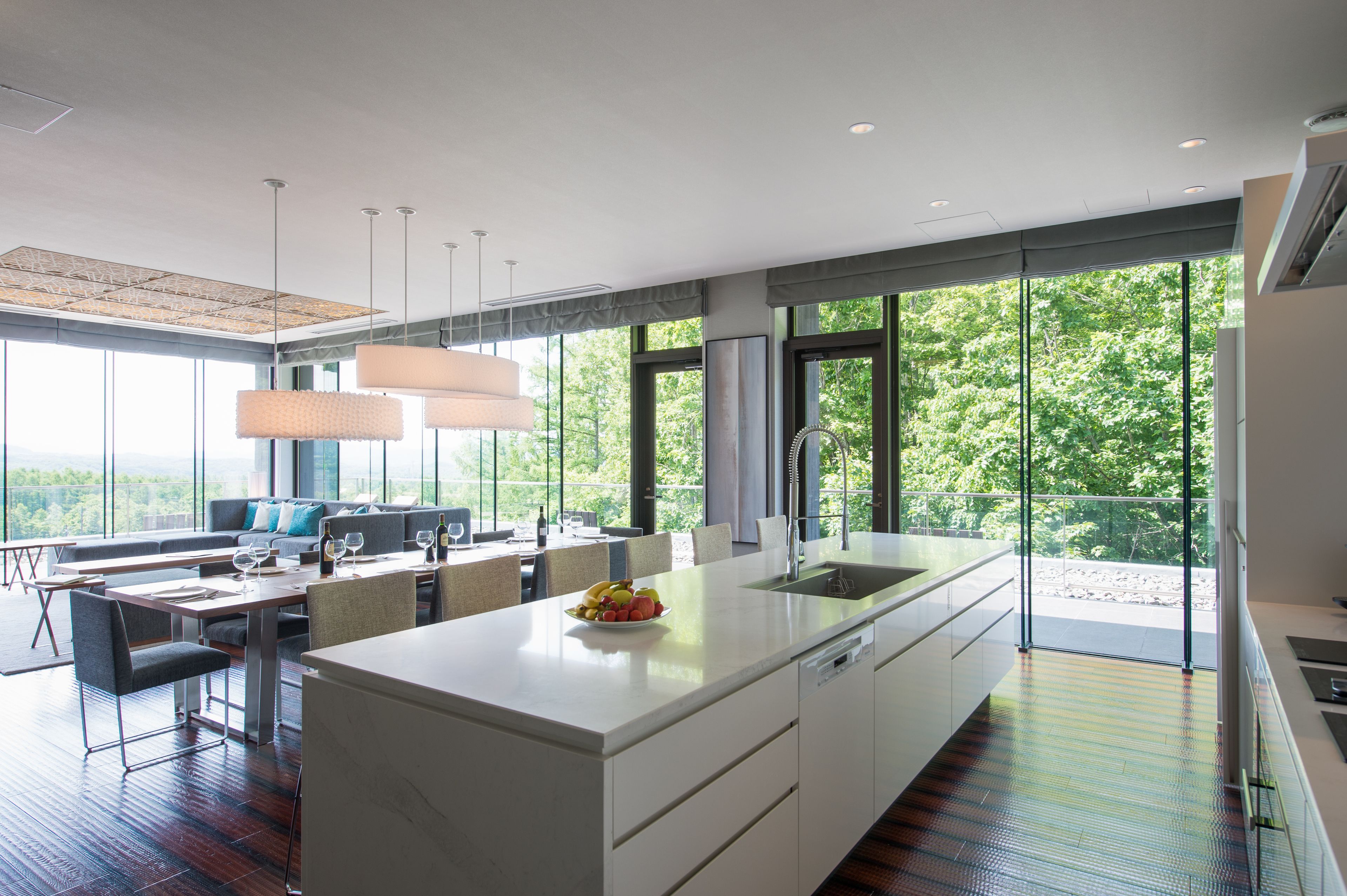 Une cuisine moderne dotée d’un grand îlot central, d’un coin repas et offrant une vue sur la verdure.