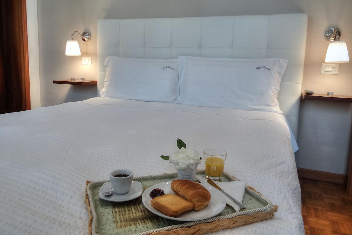 Un lit bien fait, avec des draps blancs, un plateau avec des croissants, une tasse de café et un verre de jus d’orange posés sur le lit.