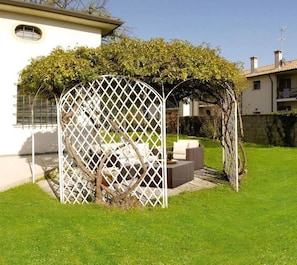 A white house with a white lattice structure in the garden, a tree, and a patio with outdoor furniture. - B&B Villa Griselda (Quinto di Treviso)