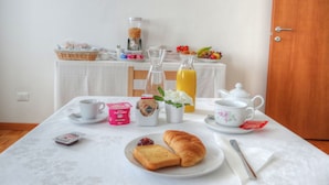 Una mesa de desayuno con pan, mermelada, una botella de jugo y una cafetera.