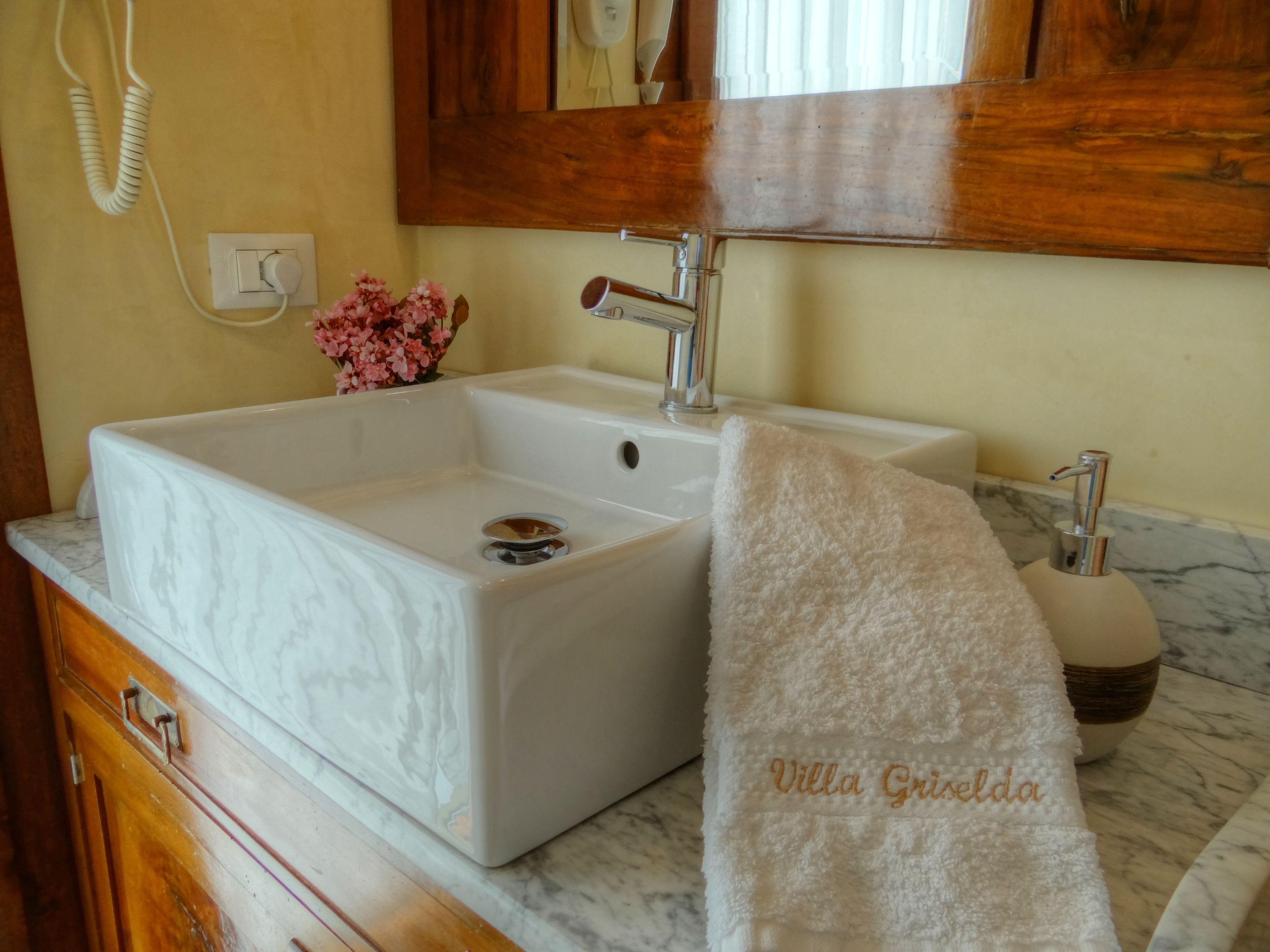 Un baño con lavamanos de mármol blanco, un mueble de madera, una toalla y un espejo sobre el lavamanos.