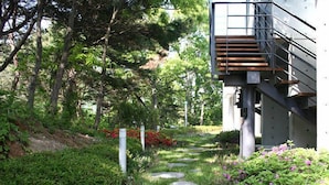 Un sendero conduce a un edificio moderno con una escalera de metal y una terraza de madera.