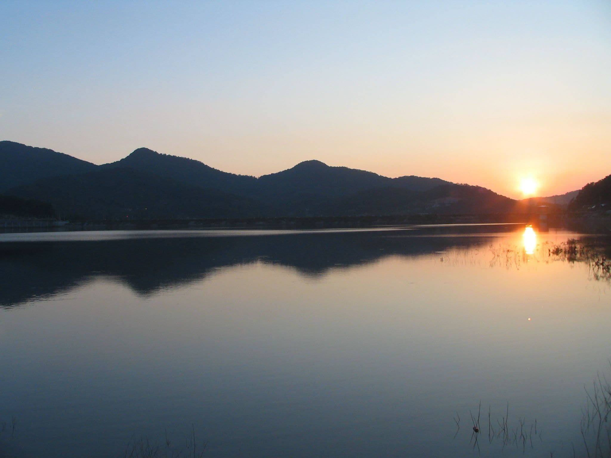 Un lago tranquilo al atardecer con montañas al fondo.