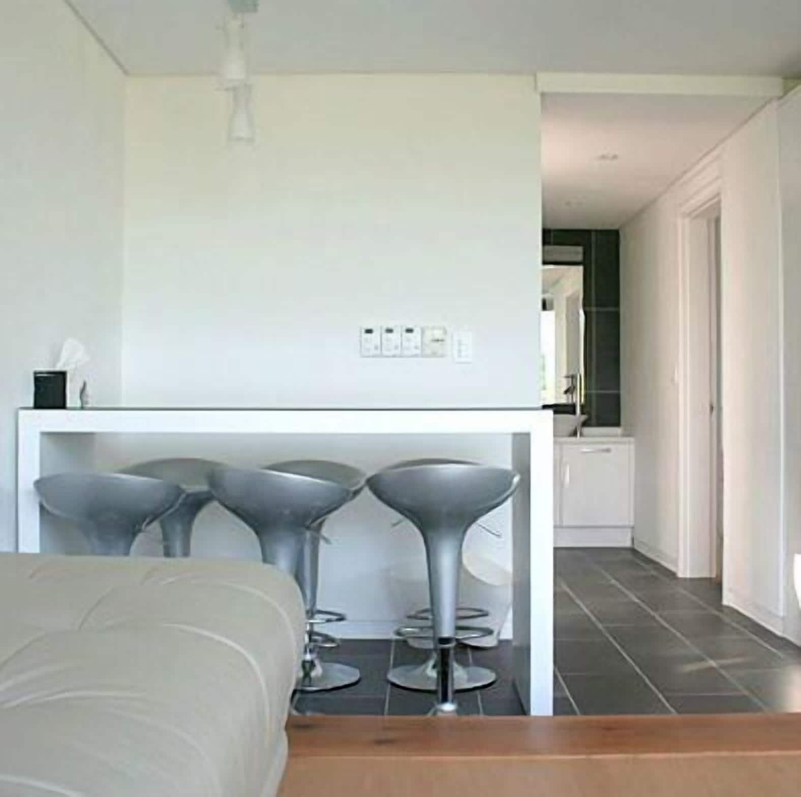 Una cocina moderna con encimera blanca, tres taburetes grises y una mesa de comedor blanca.