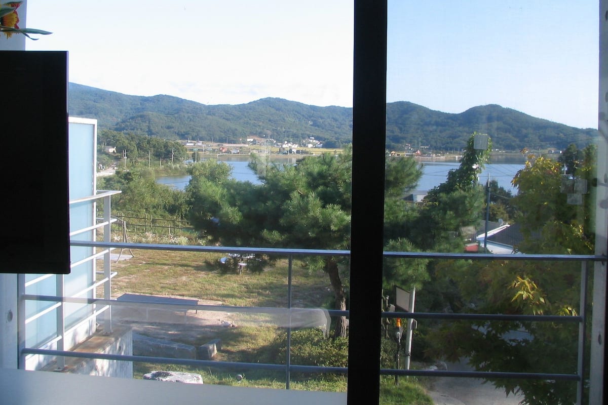 A view from a window overlooking a lake, mountains, and a small town.