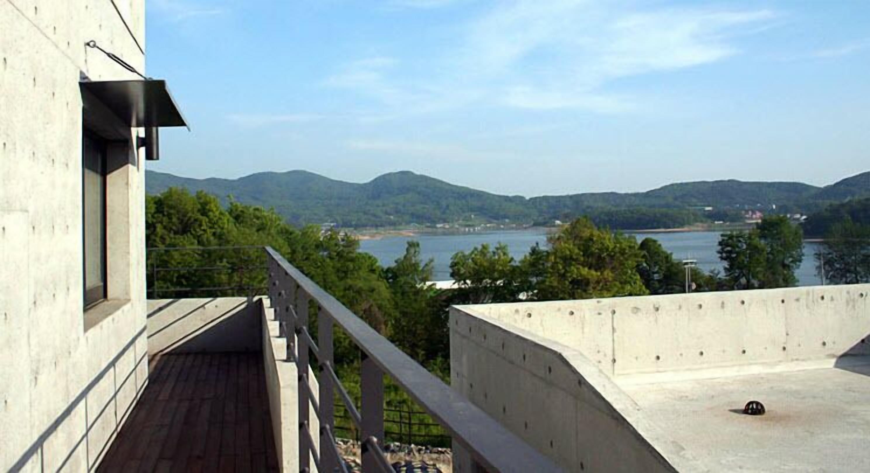 Un bâtiment moderne doté d’un balcon donnant sur un lac et des collines.