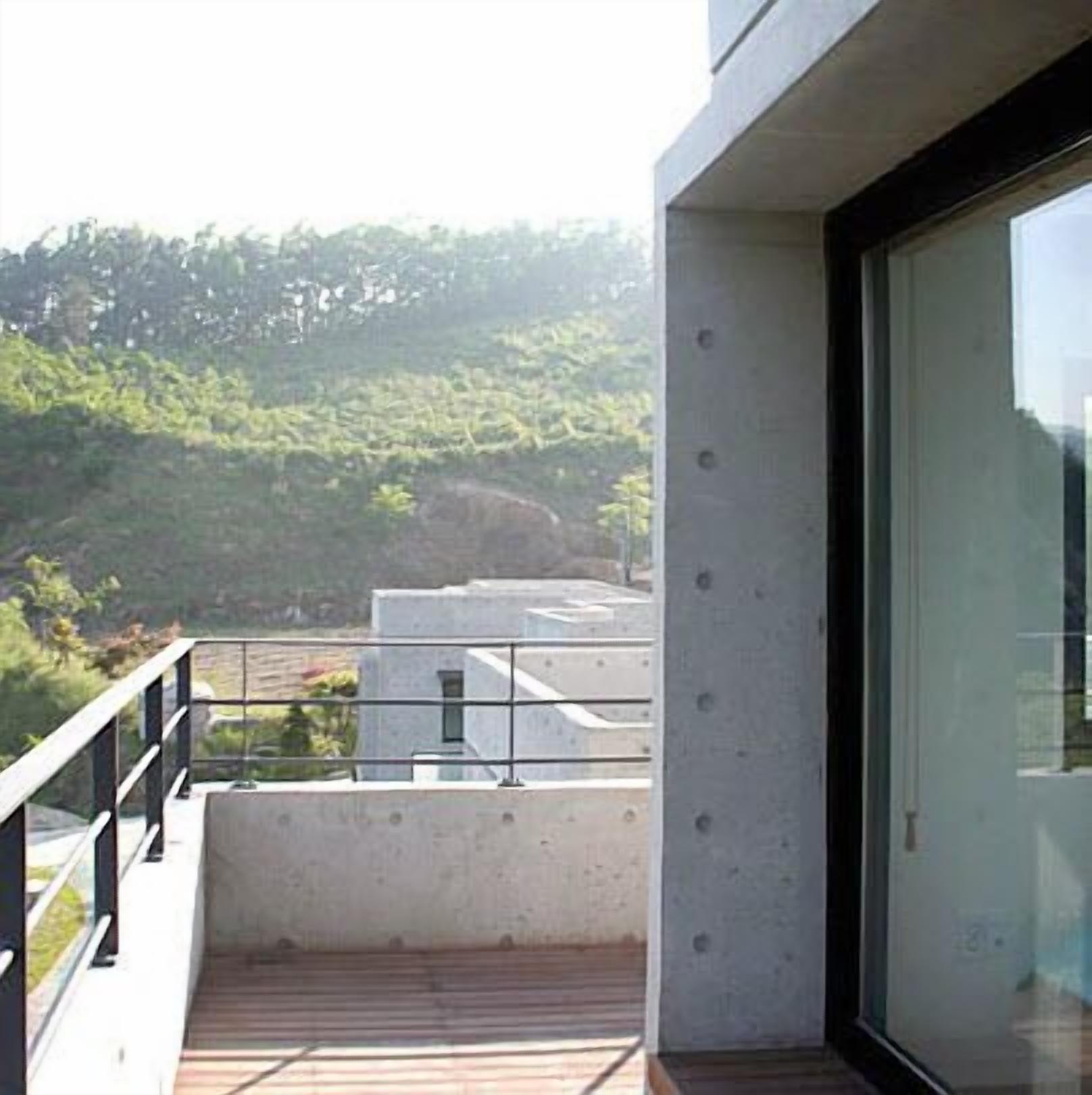 Een modern balkon met een houten vloer en metalen hekwerk, met uitzicht op een glooiend landschap.