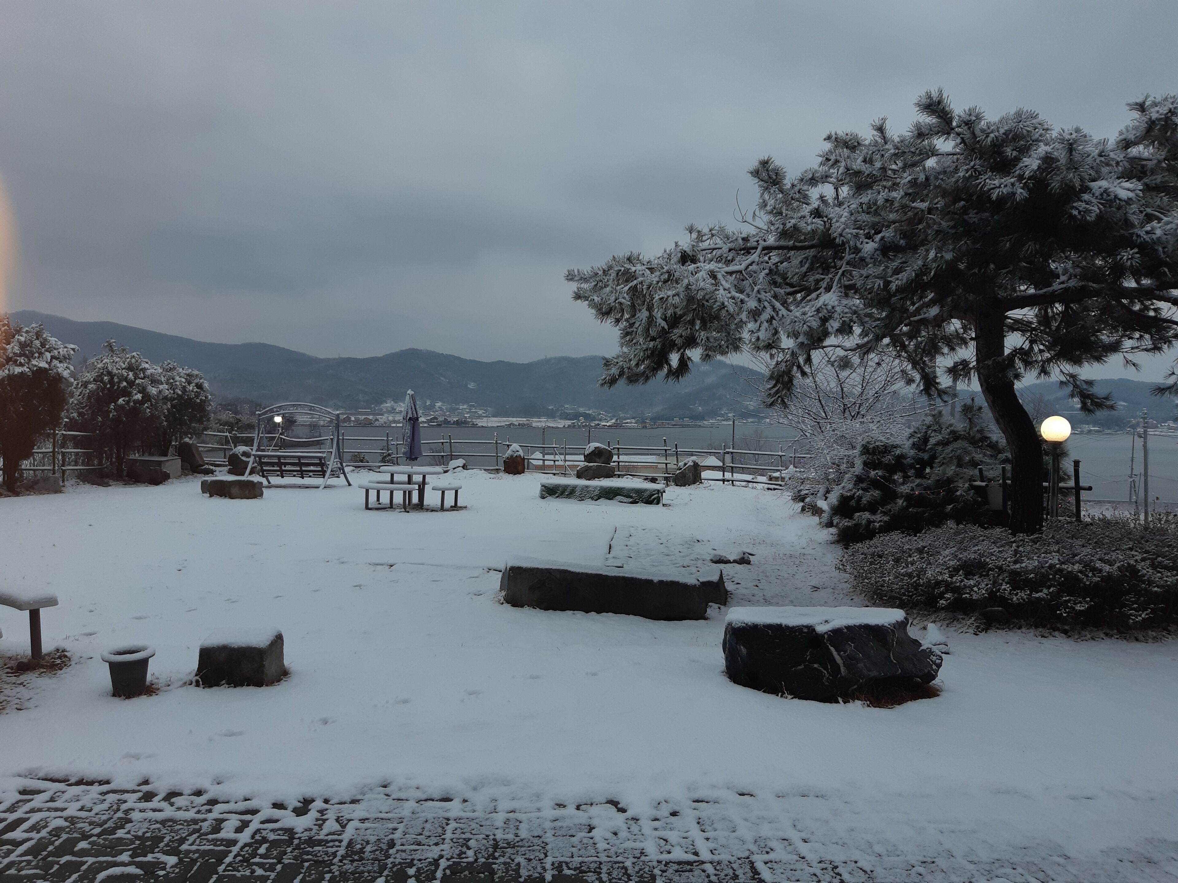 Área externa coberta de neve, com bancos e um poste de luz.