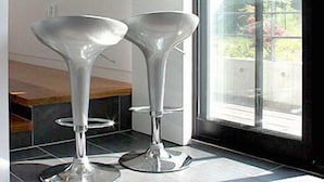 Una cocina moderna con dos taburetes altos y metálicos de forma de embudo, y un ventanal con vistas a zonas verdes.