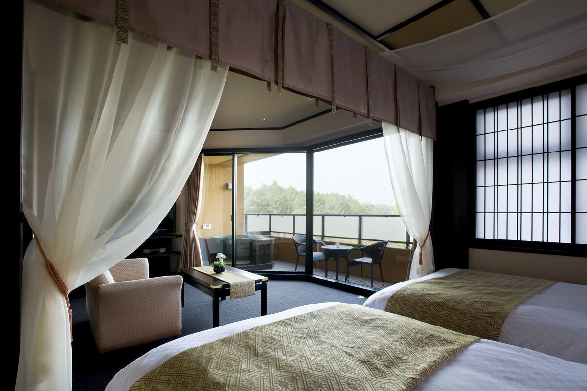 Habitación de hotel con dos camas, un balcón con mesa y sillas, y vistas al exterior.