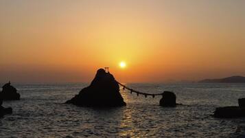 A sunset over a calm sea with a rock formation in the center and a rope bridge leading to it.