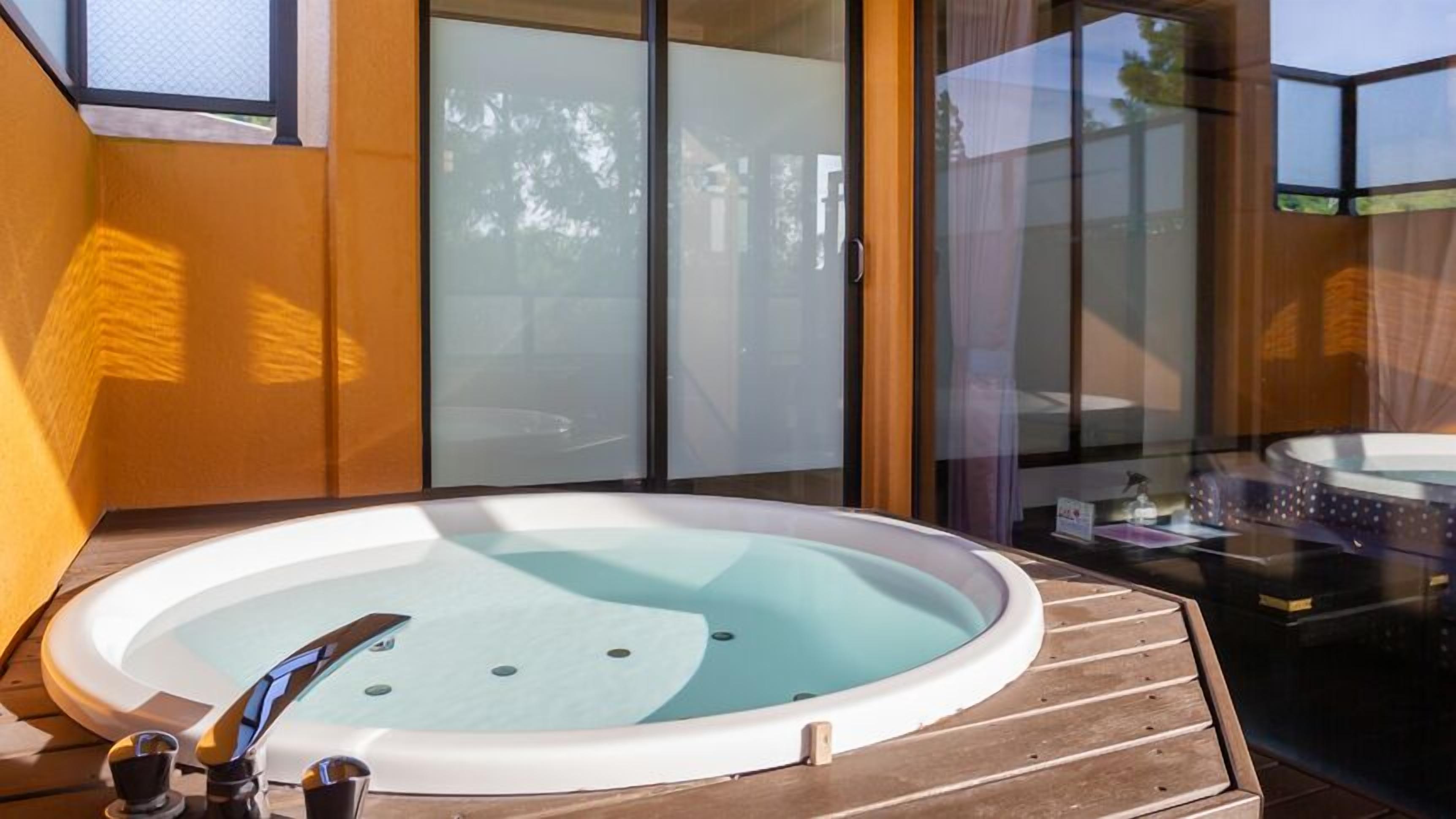 Un jacuzzi en una terraza de madera, con un muro de vidrio y puertas correderas al fondo.