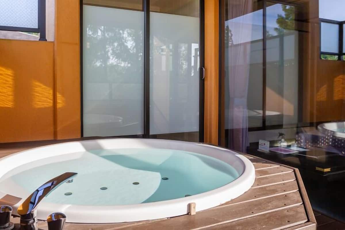 Un jacuzzi en una terraza de madera, con un muro de vidrio y puertas correderas al fondo.
