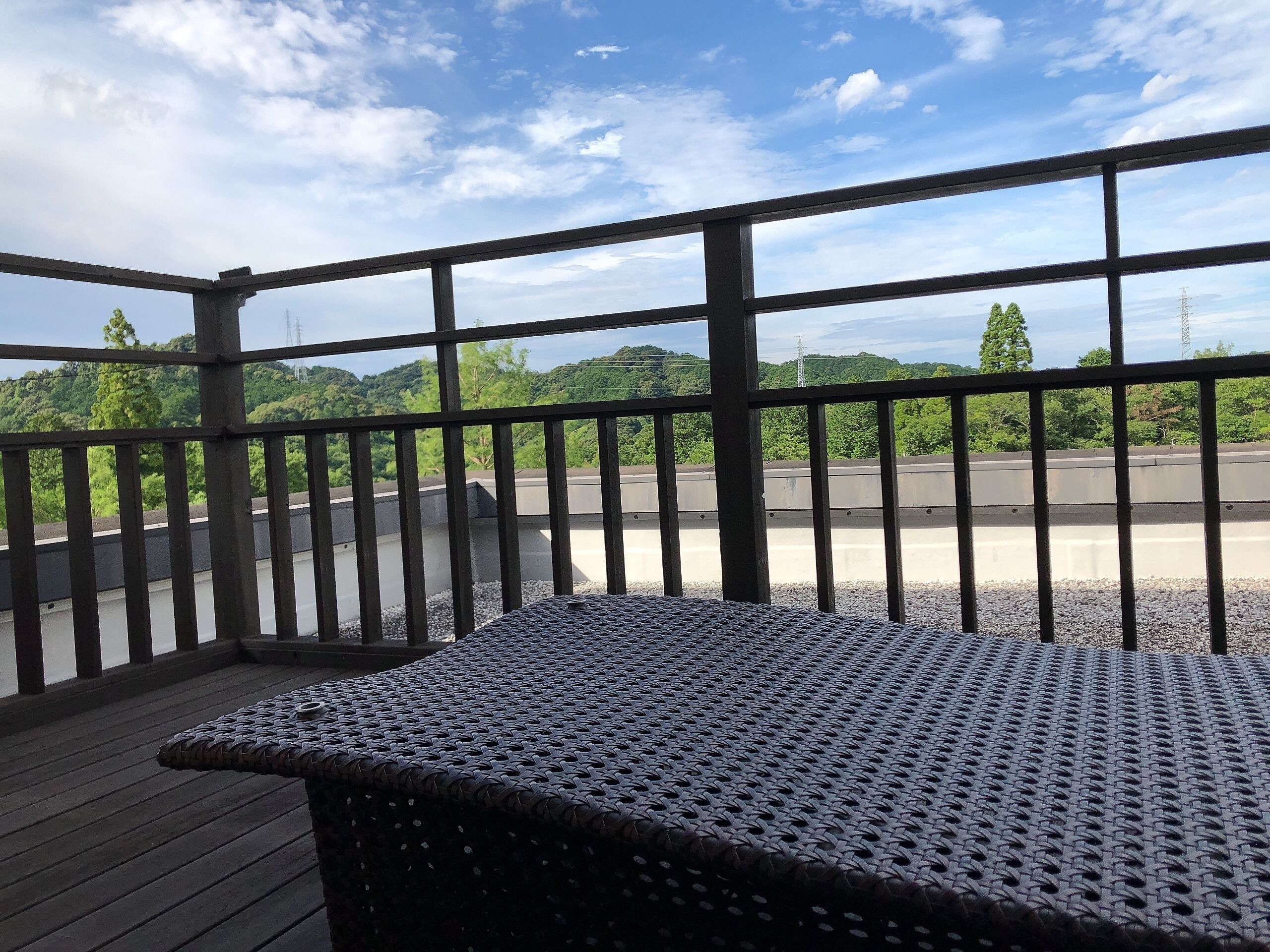 A balcony with a metal railing, a woven table, and a view of a road and greenery.