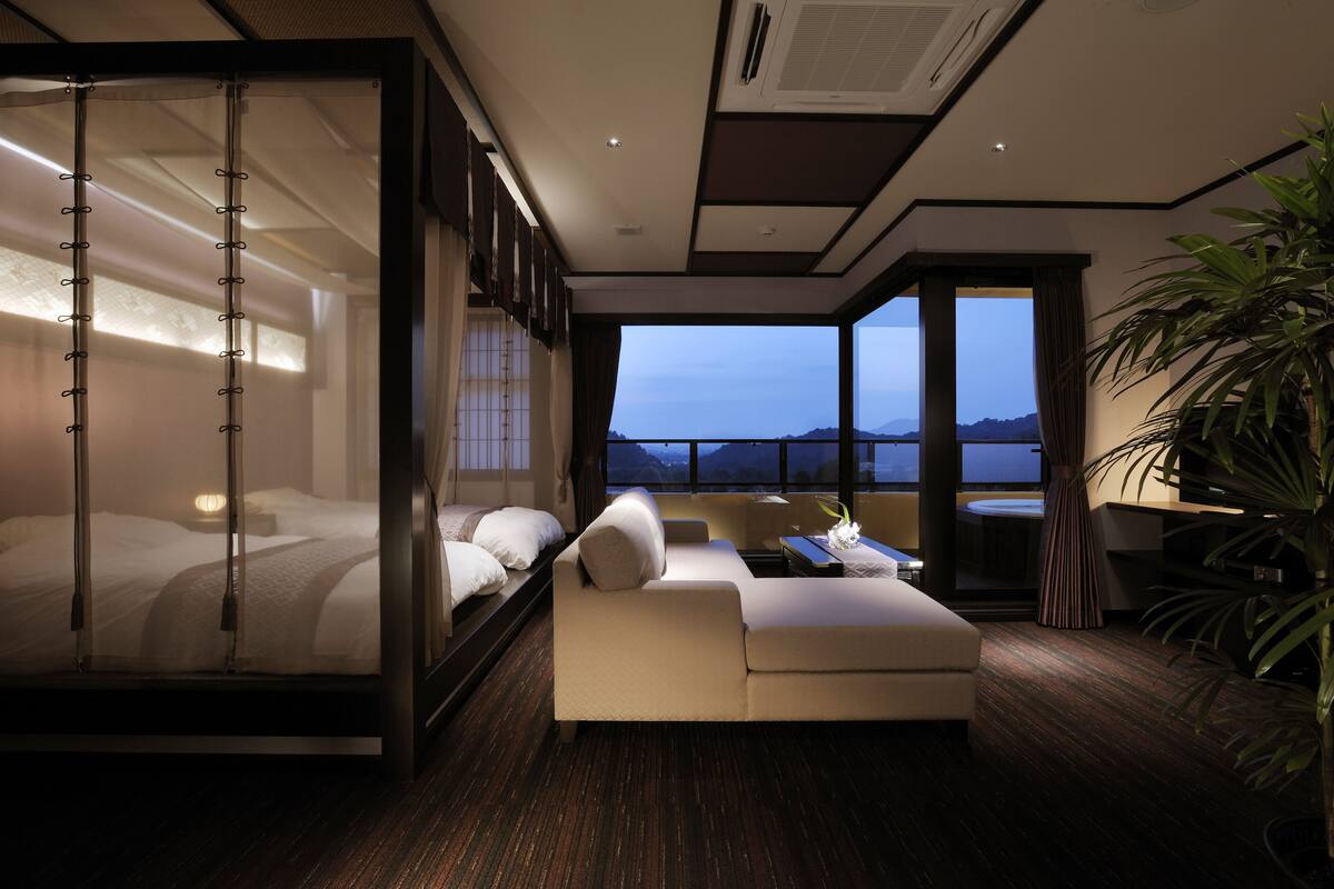 Una habitación de hotel moderna con balcón, una cama, un sofá y zona de comedor.