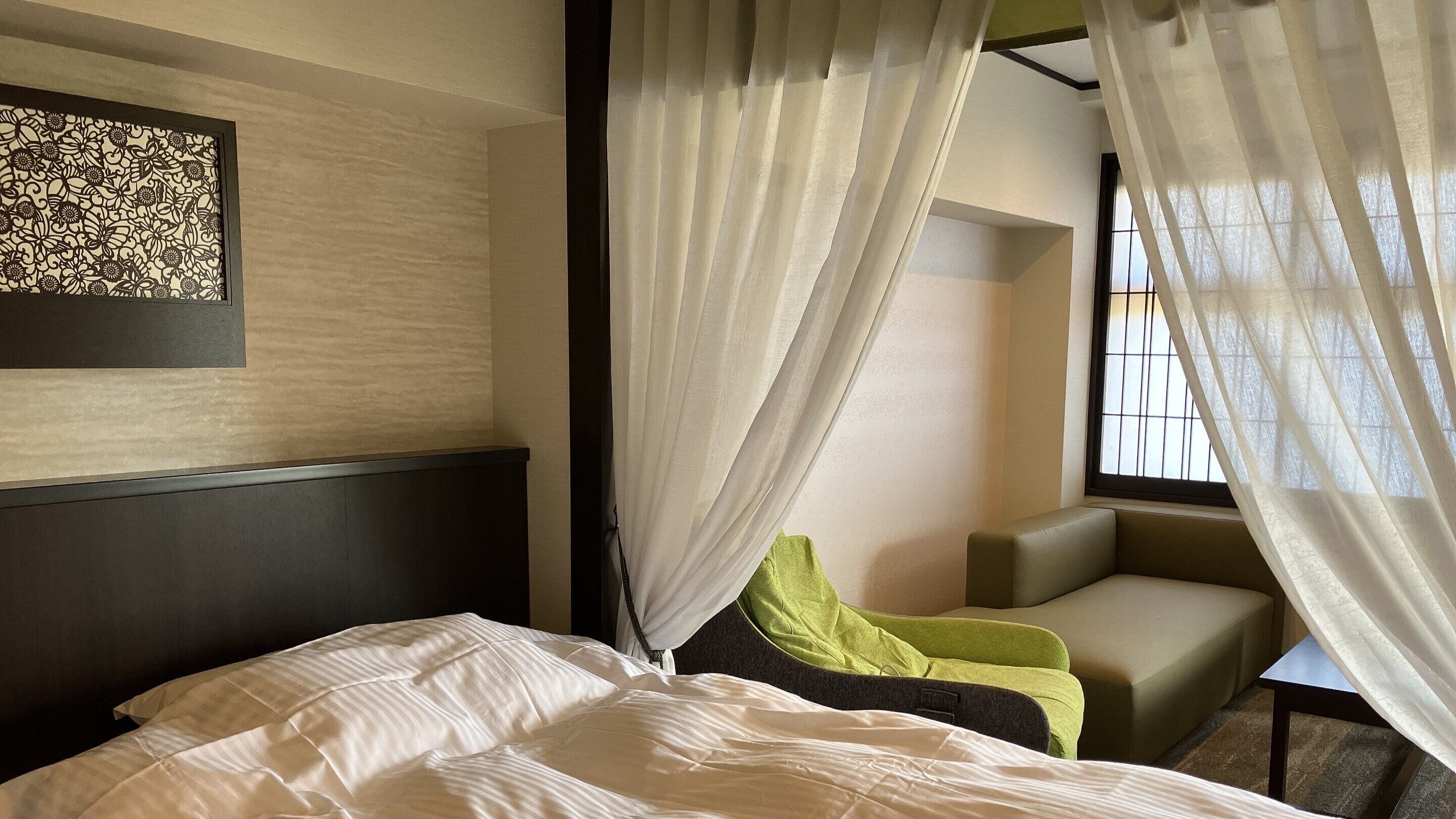 Una habitación de hotel con cama, una silla, una mesita y una ventana con cortinas.
