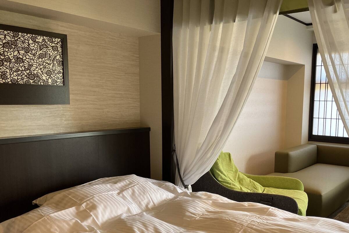 Una habitación de hotel con cama, una silla, una mesita y una ventana con cortinas.
