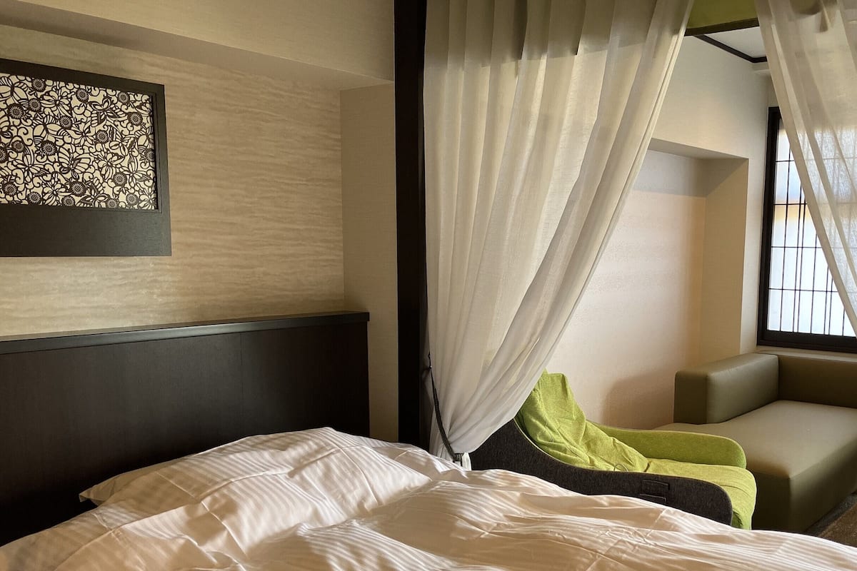 Una habitación de hotel con cama, una silla, una mesita y una ventana con cortinas.