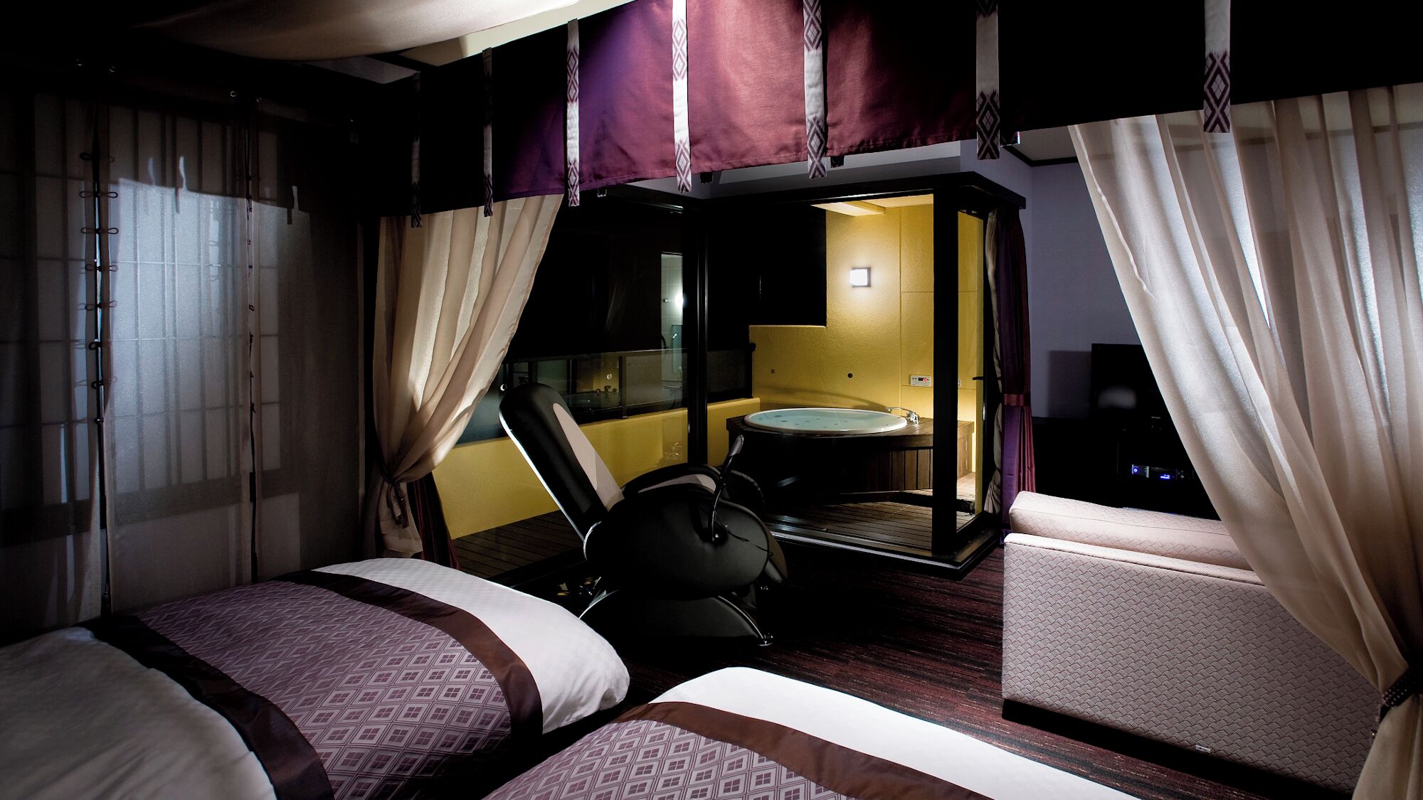 A hotel room with two beds, a small table, a chair, and a bathroom visible through an open door.