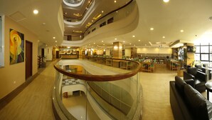 Um átrio de vários níveis com guarda-corrimão de vidro central, área de refeições e espaço de estar com sofás.