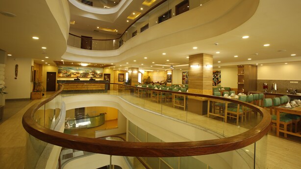 Um hall de hotel com vários níveis, corrimão de vidro, áreas de estar e um balcão de recepção central.