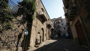 Una estrecha calle adoquinada con edificios de piedra, una señal de calle visible y un coche estacionado.