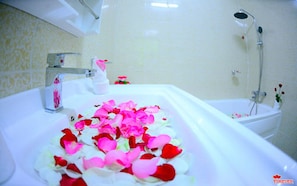 A bathroom with a bathtub filled with rose petals, a shower, and a sink with a bottle of soap. - Vega Star Hotel (Yangon)