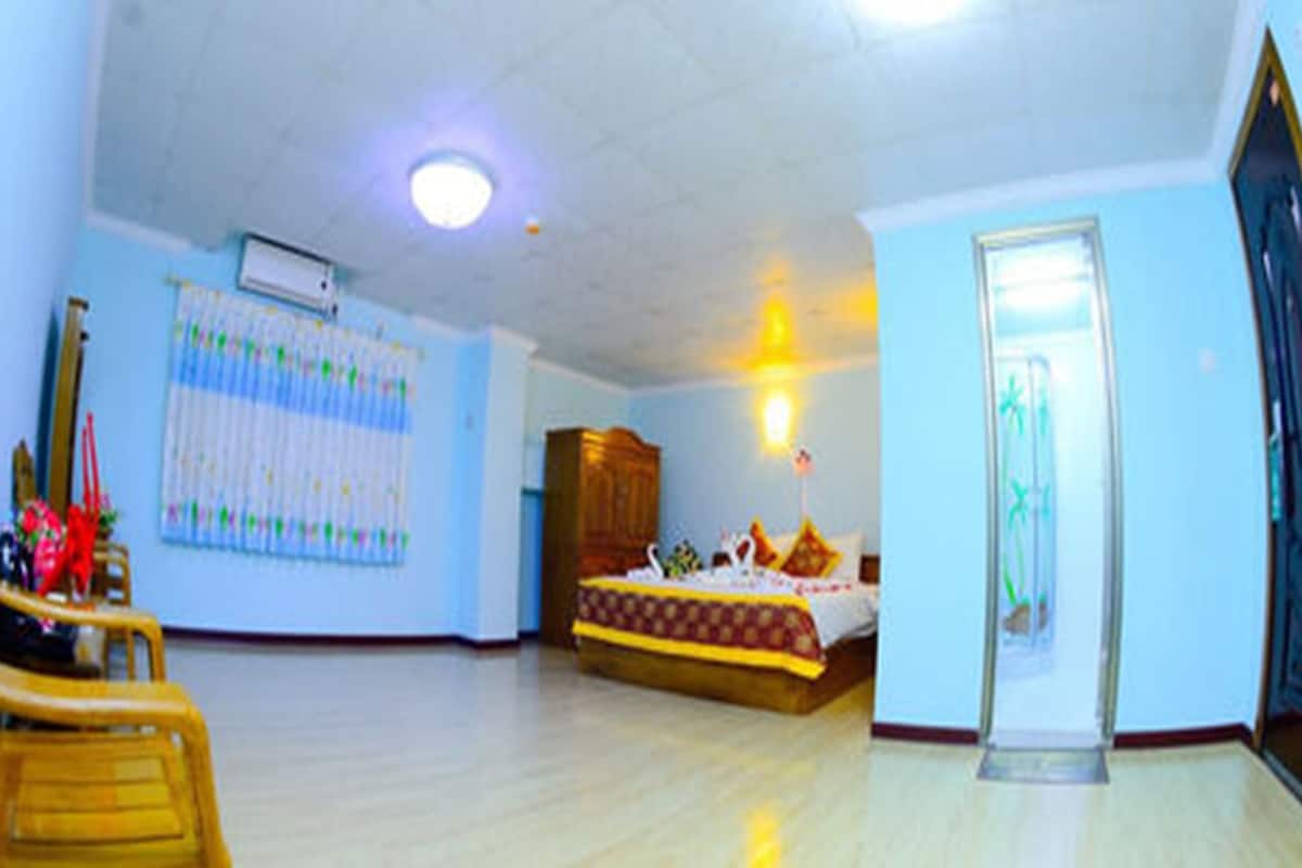 A spacious room with a wooden floor, a bed with a patterned bedspread, a wooden cabinet, and a wall-mounted air conditioning unit.