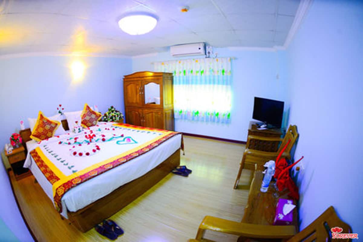 A bedroom with a bed, a television, a wooden wardrobe, and a window with curtains.